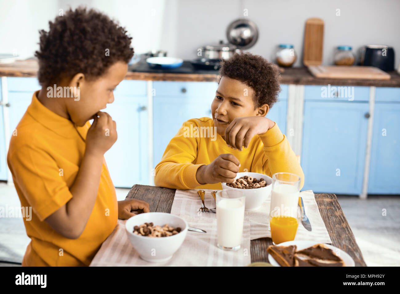 Curly-pelose ragazzi piccoli chattare mentre mangia cereali Foto Stock