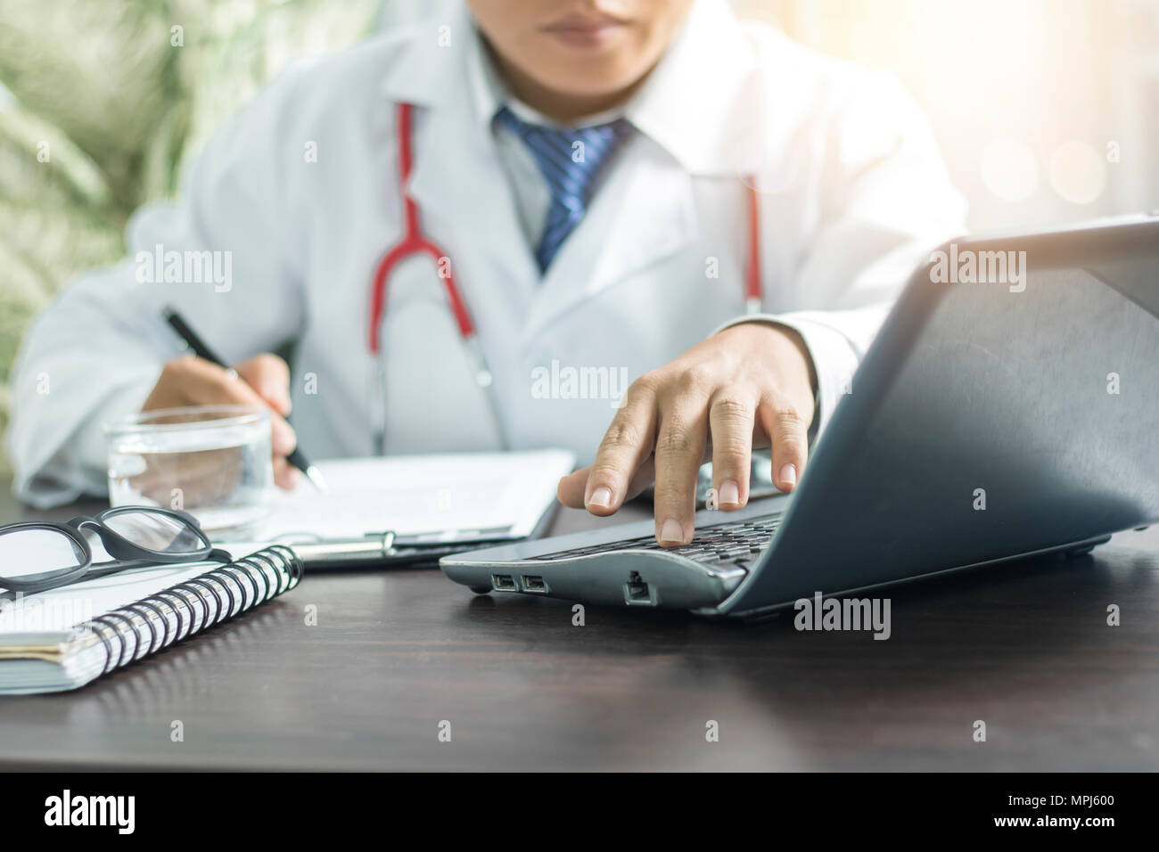 Medico nella ricerca di informazioni dal computer e la scrittura su notebook sul tavolo di lavoro Foto Stock