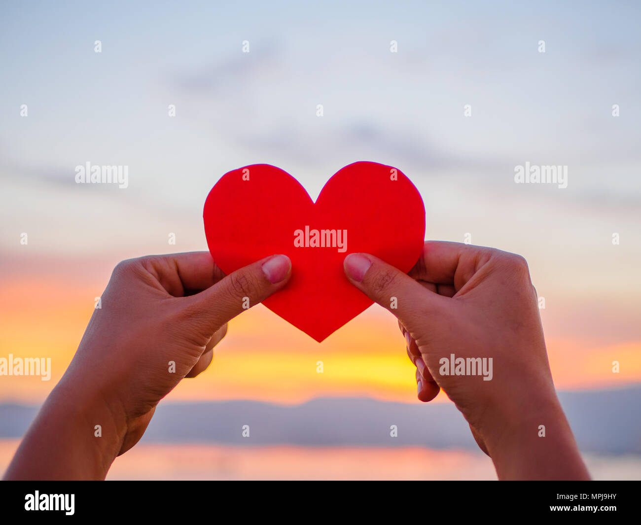 La mano si solleva la carta rossa cuore con blur la luce del sole durante il tramonto, il giorno di San Valentino Foto Stock