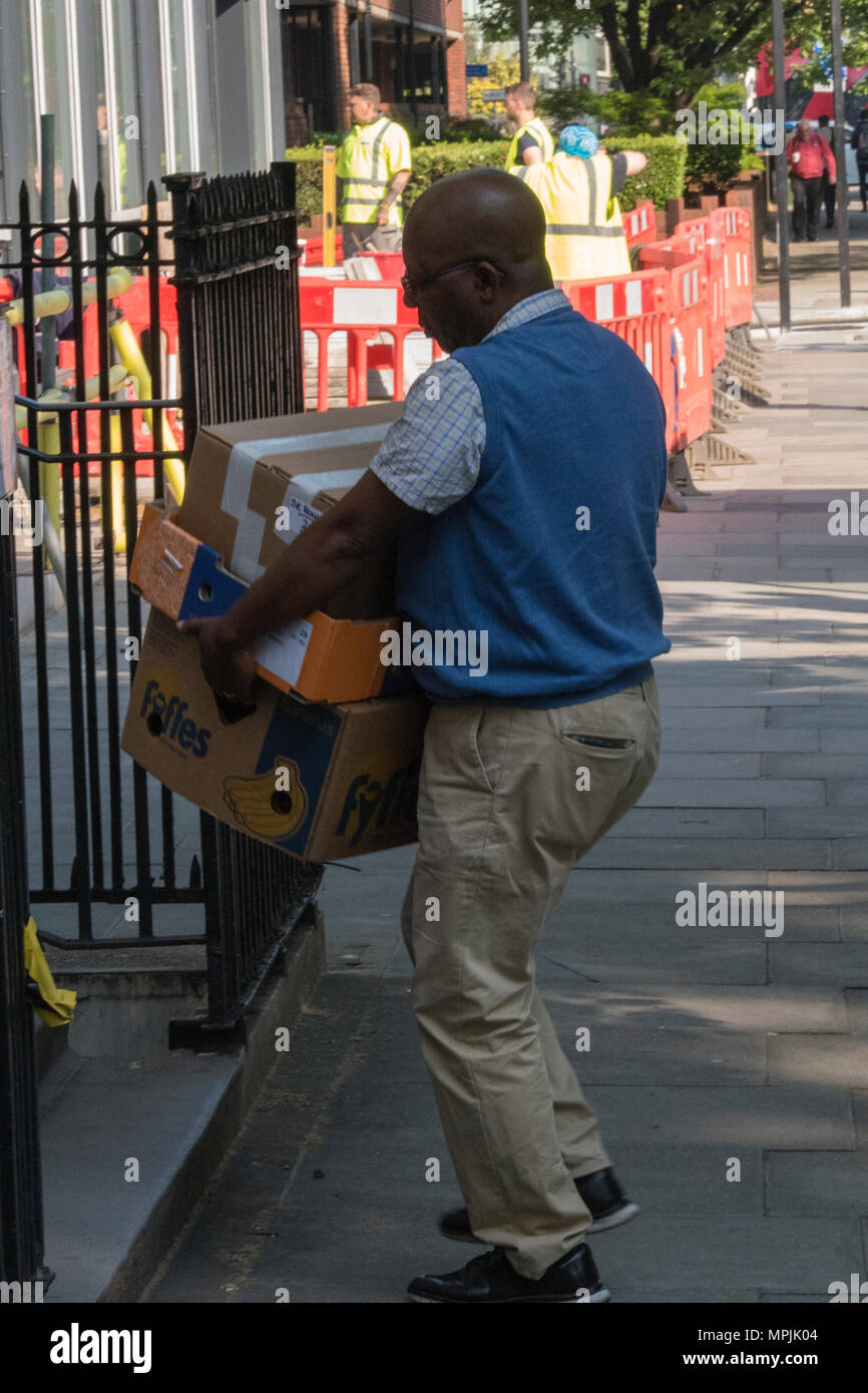 Un uomo di etnia afro-caraibica portando una pila di scatolato e la consegna dei pacchi di indirizzo nel centro di Londra. Il sollevamento di carichi pesanti consegna uomo su turni. Foto Stock