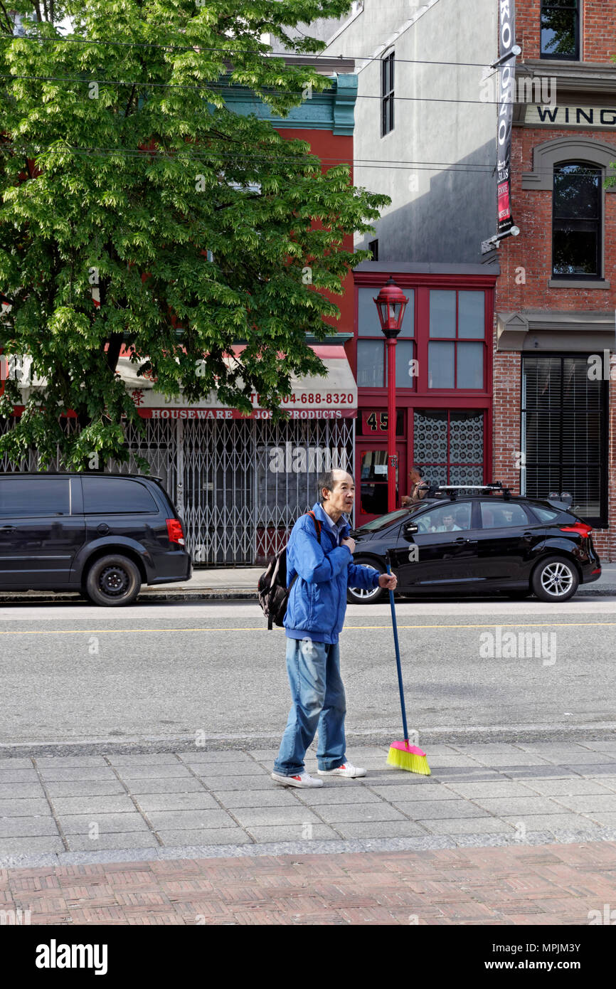 Anziani uomo cinese che trasportano un colorato scopa in Chinatown, Vancouver, BC, Canada Foto Stock