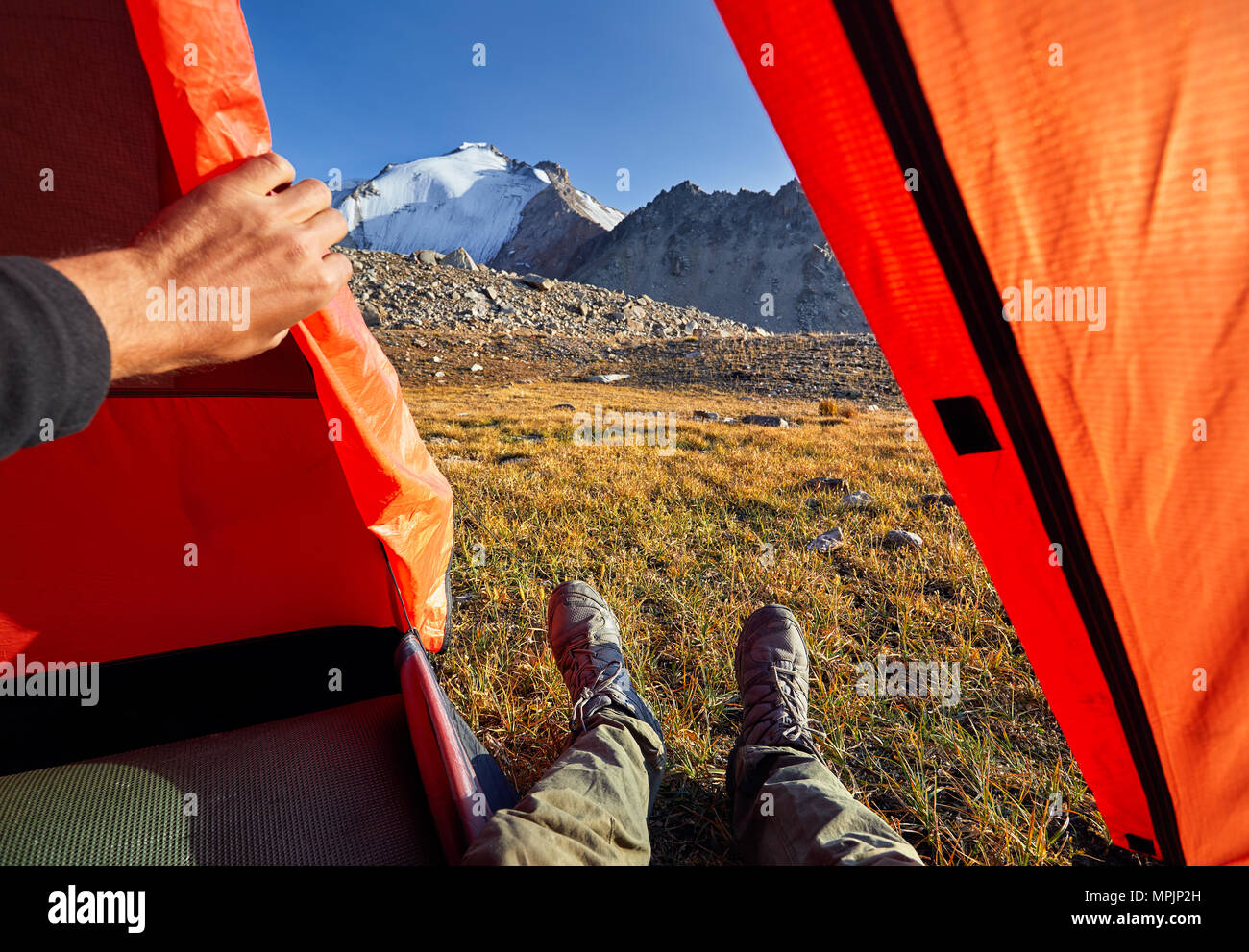 Escursionista gambe dalla tenda arancione con la vista bella vertice nevoso Foto Stock
