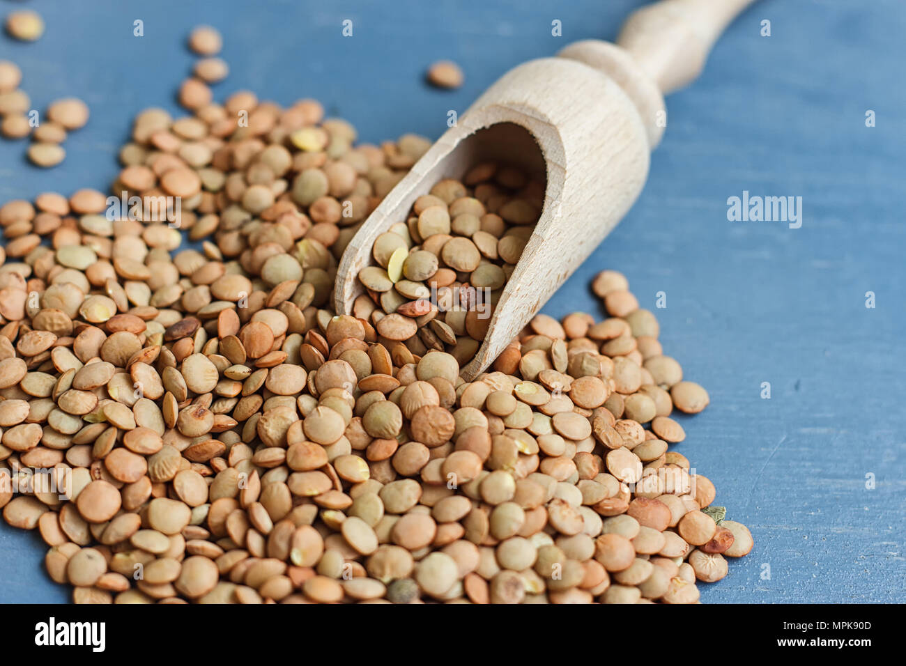 Materie lenticchie su un cucchiaio di legno su uno sfondo blu Foto Stock