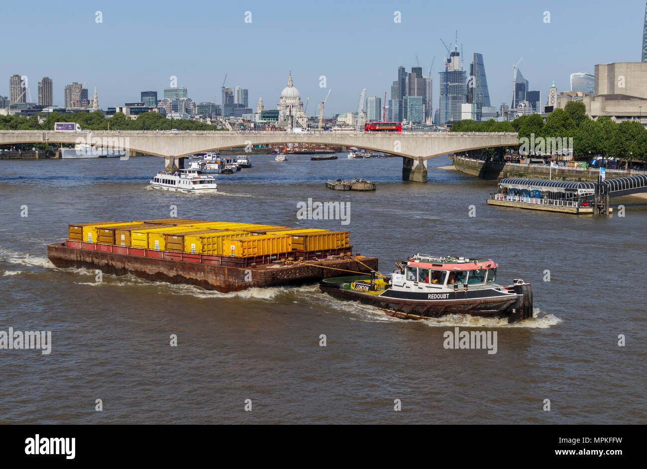 Cory Riverside tug 'Redoubt' il traino di una chiatta caricato con il giallo dei contenitori lungo il fiume Tamigi sopra il ponte di Waterloo, London, Regno Unito Foto Stock