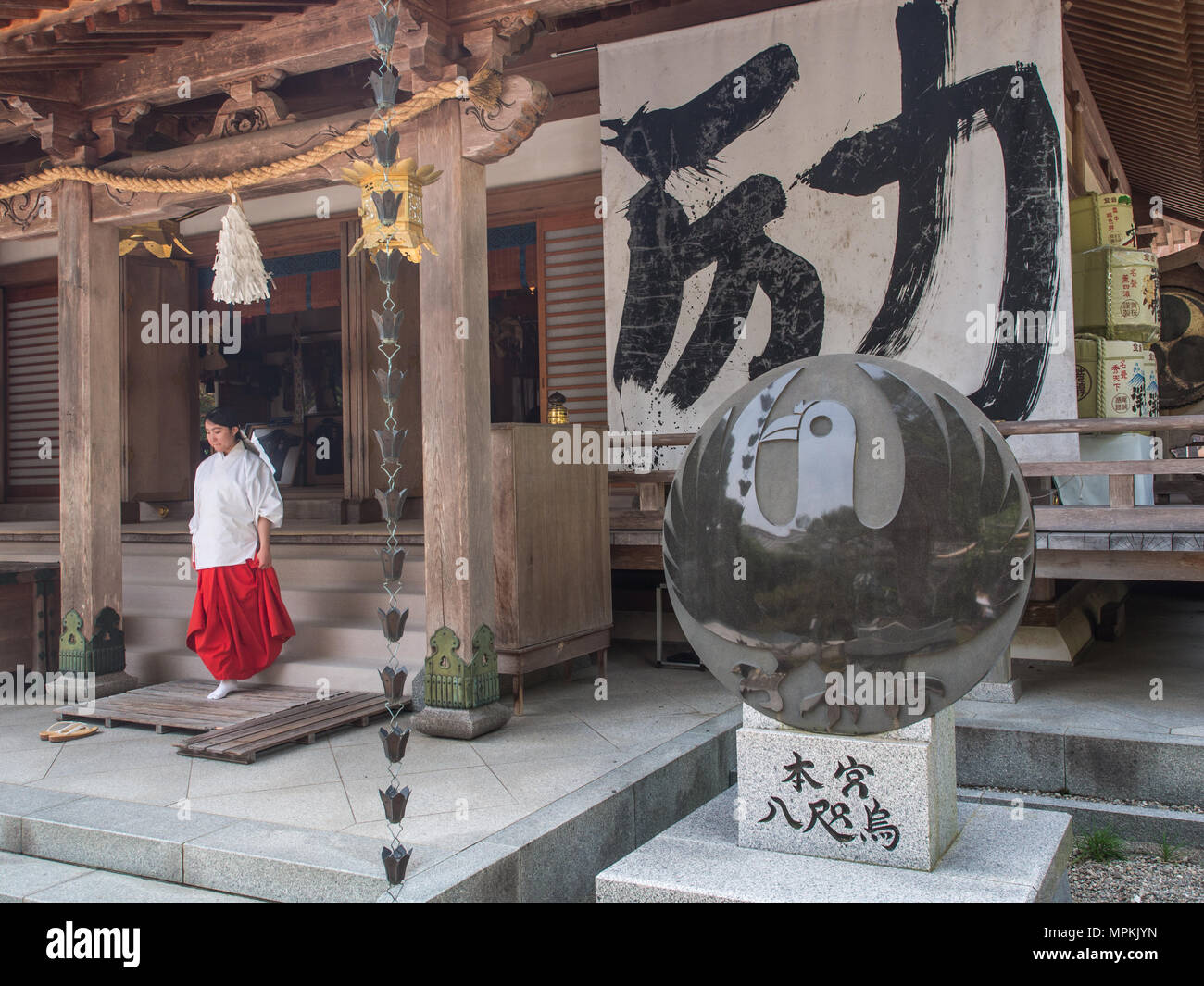 Donna in tradizionali shinto costme a Haiden, Hall di culto. Yatagarasu, a tre gambe crow simbolo, sul disco di pietra. Kumano Hongu Taisha, Wakayama P Foto Stock