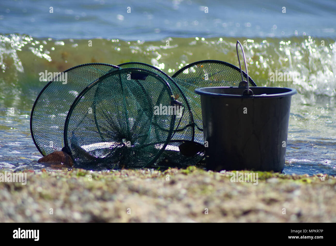 Una rete da pesca con pesci e una benna sono in piedi sulla spiaggia. Una splendida wave può essere visto in background. Foto Stock