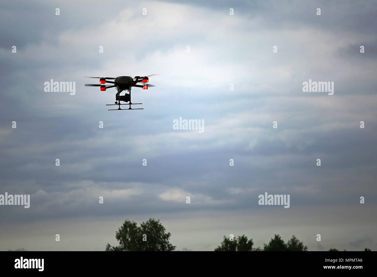 Un quadcopter drone in volo sopra le cime degli alberi contro la moody sky. Foto Stock