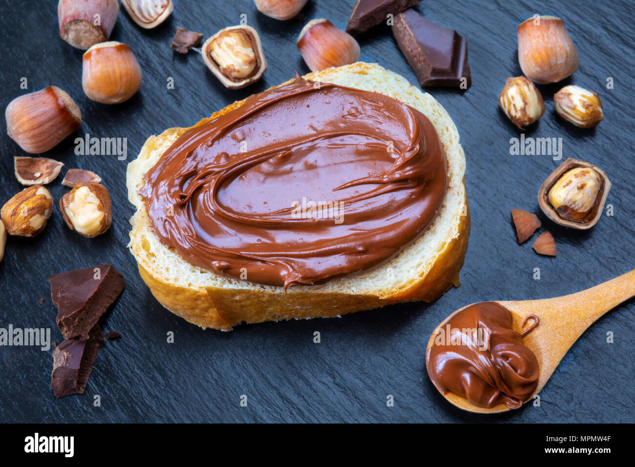 Fetta di pane con il diffondersi di crema di cioccolato e nocciole sulla tavola nera. Serve una deliziosa colazione concetto. Foto Stock