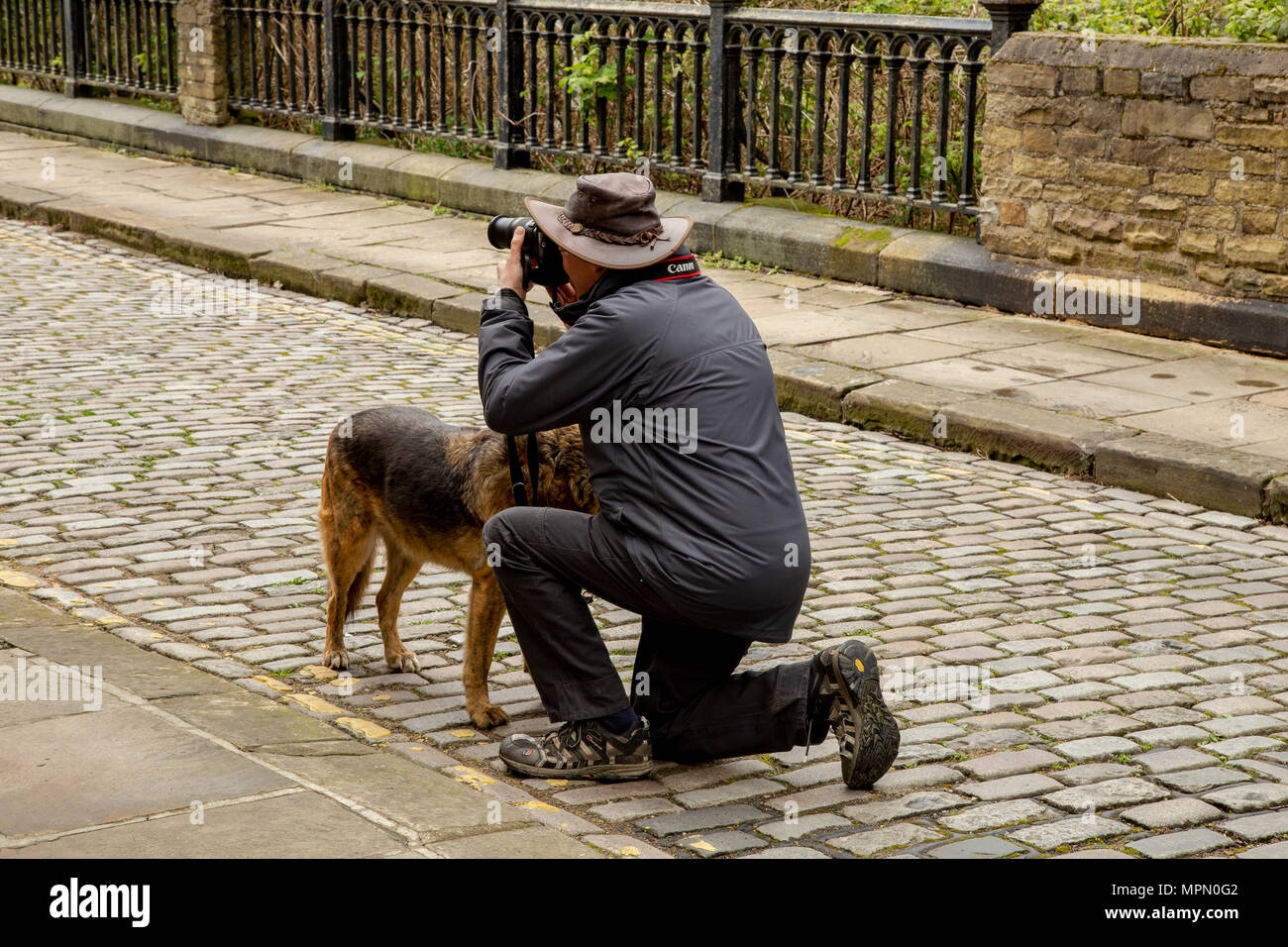 Un uomo si inginocchia per scattare una fotografia in Saltair, Yorkshire. Il suo cane sorge accanto a lui. Foto Stock
