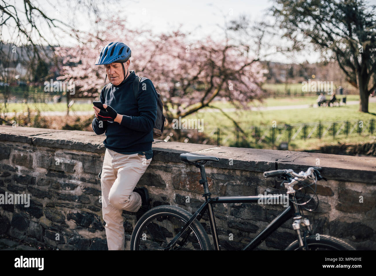 L'uomo anziano con il ciclismo casco utilizza lo smartphone Foto Stock