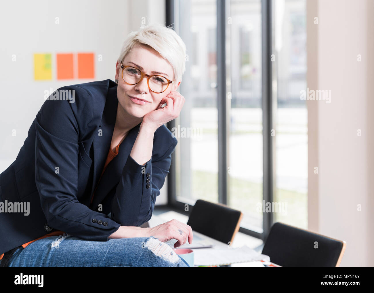 Ritratto di fiducioso imprenditrice seduta sul tavolo in ufficio Foto Stock