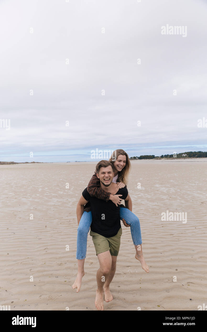 Francia, Bretagna Guisseny, felice giovane ragazza portante piggyback sulla spiaggia Foto Stock
