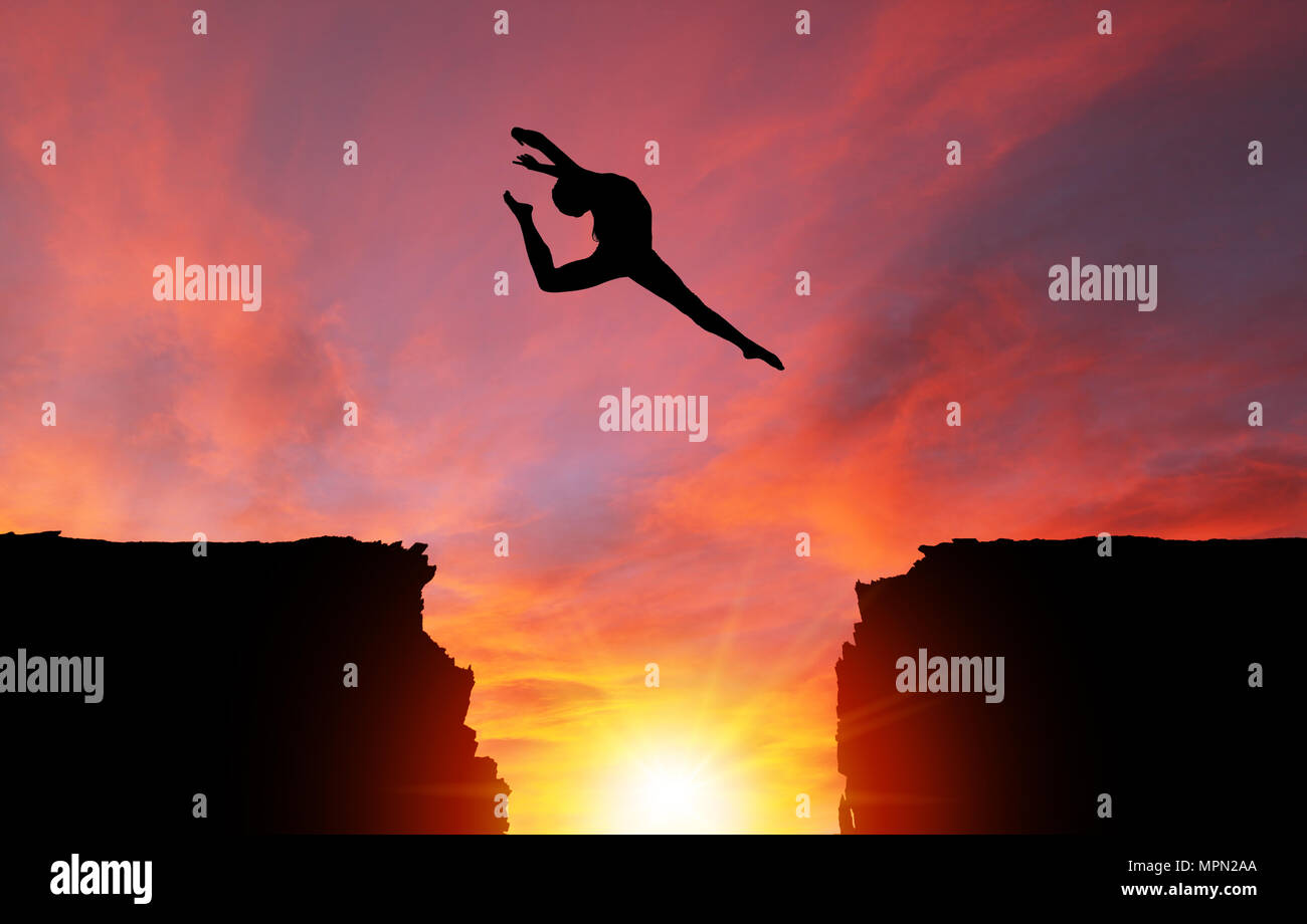 Silhouette di una ragazza ballerino in un cervo split leap su scogli pericolosi con drammatico tramonto o l'alba di sfondo e copiare lo spazio. Concetto di fede, conq Foto Stock