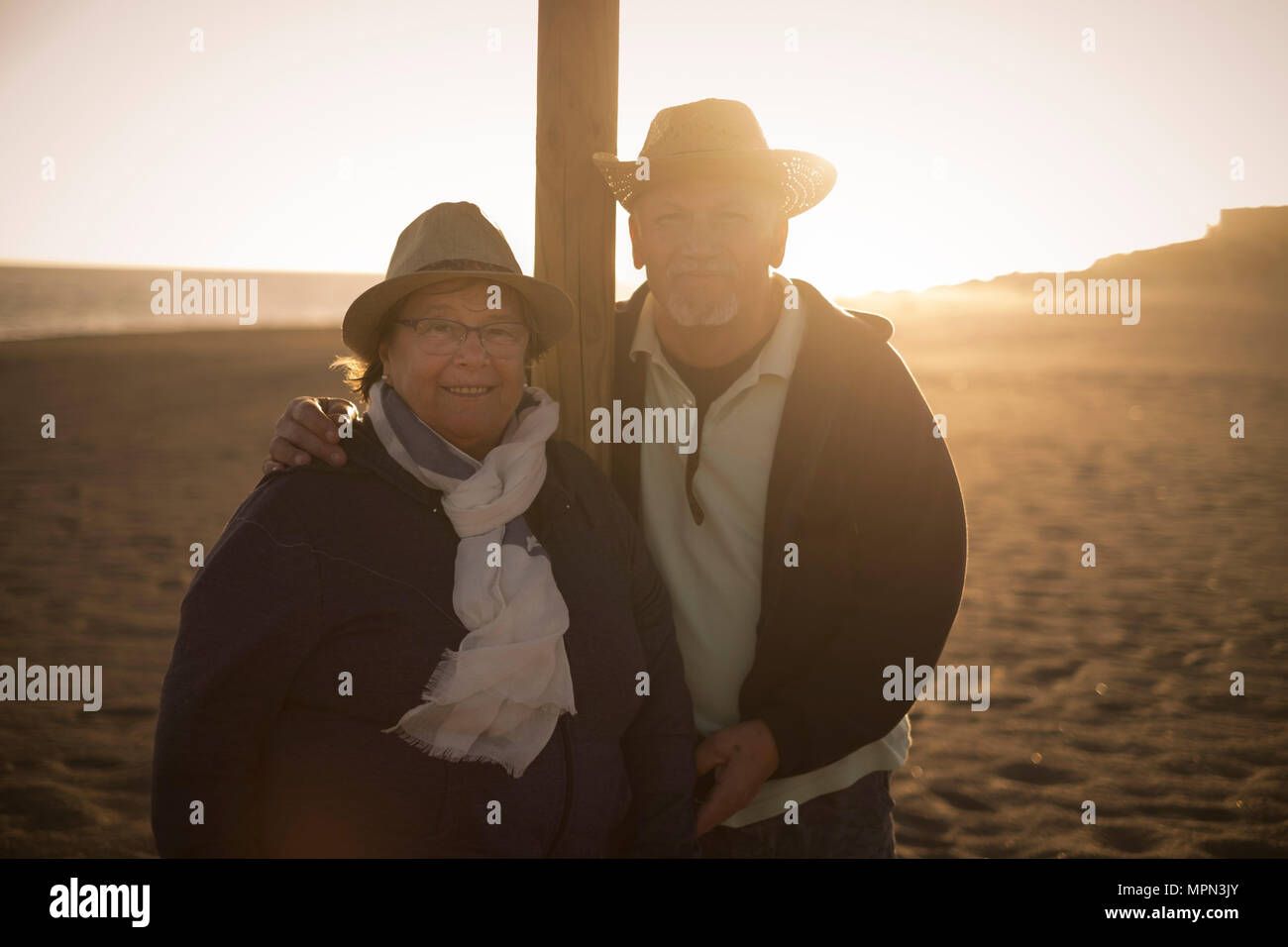 L uomo e la donna senior di età soggiorno sulla spiaggia con retroilluminazione bello dal tramonto. indossare cappelli e amore per sempre insieme concetto Foto Stock