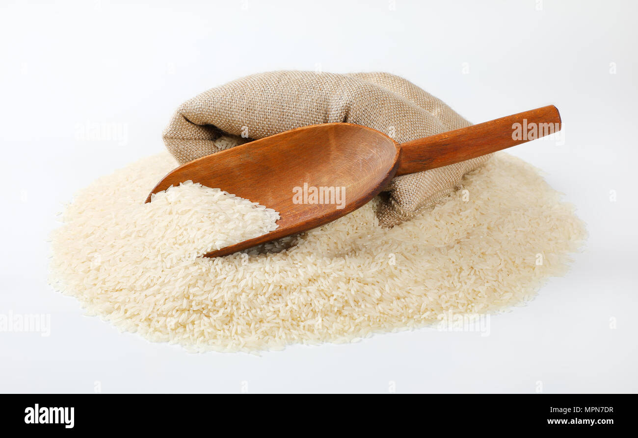 Pila di grana lunga riso, scoop di legno e tela borsa su sfondo bianco Foto Stock
