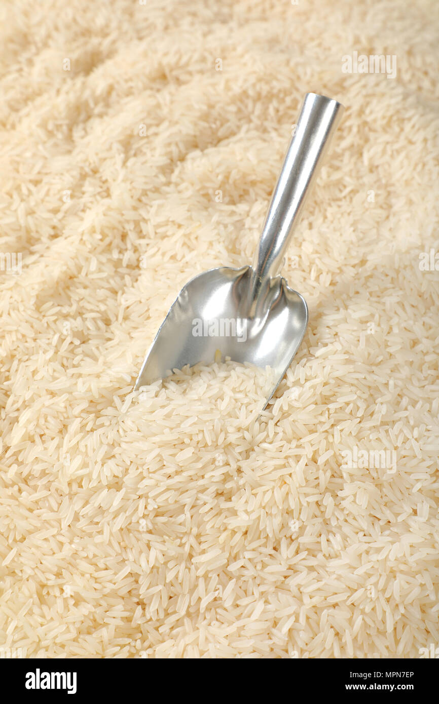 Scoop di bianco a grana lunga riso su sfondo di riso Foto Stock
