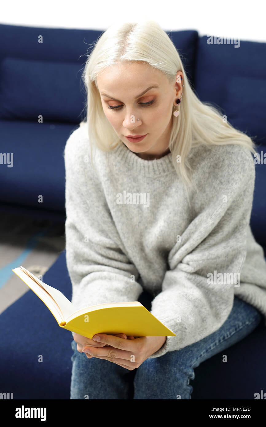 Rilassatevi con un libro. Bella bionda la lettura di un libro mentre seduti a casa Foto Stock