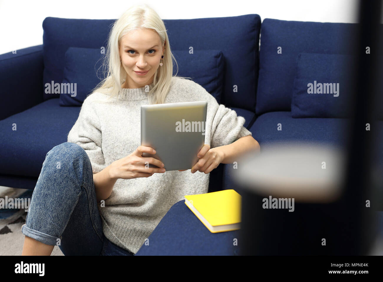 La lettura di un e-book su una tavoletta digitale. Bella partecipante di leggere ebook sul tablet mentre è seduto sul tappeto. Foto Stock