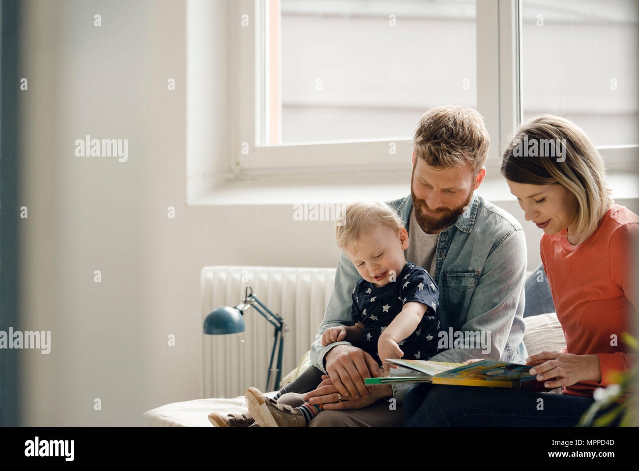 Little Boy sittiing sul padre grembo di madre la lettura di libro per bambini Foto Stock