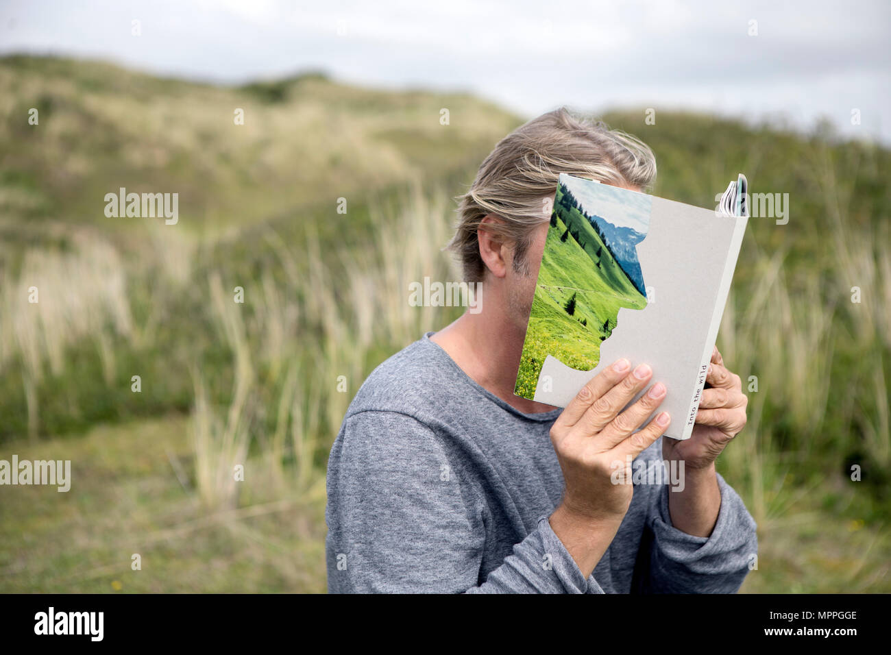 L uomo alla lettura della storia prenota nelle dune, che copre il volto Foto Stock