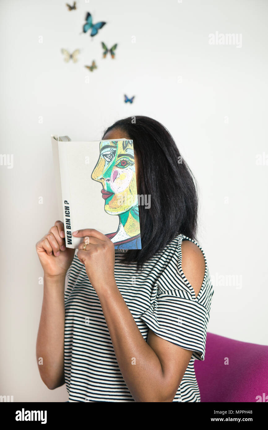 Donna che ricopre la faccia con il libro e la lettura di poesie con farfalle Foto Stock