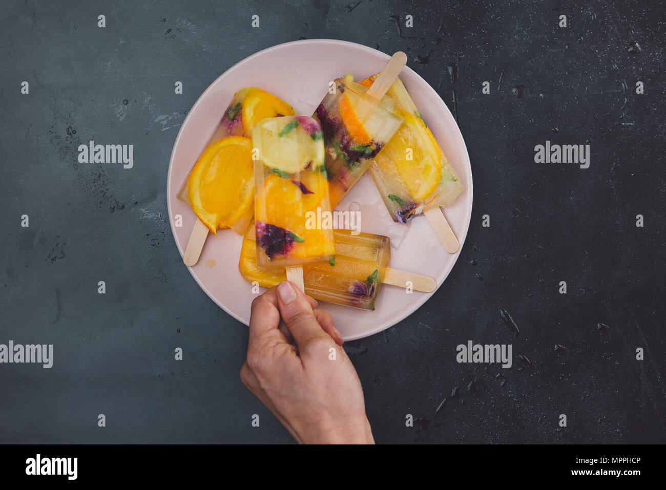 Tenendo la mano in casa arancione ghiaccioli al limone con fiori commestibili dalla piastra Foto Stock