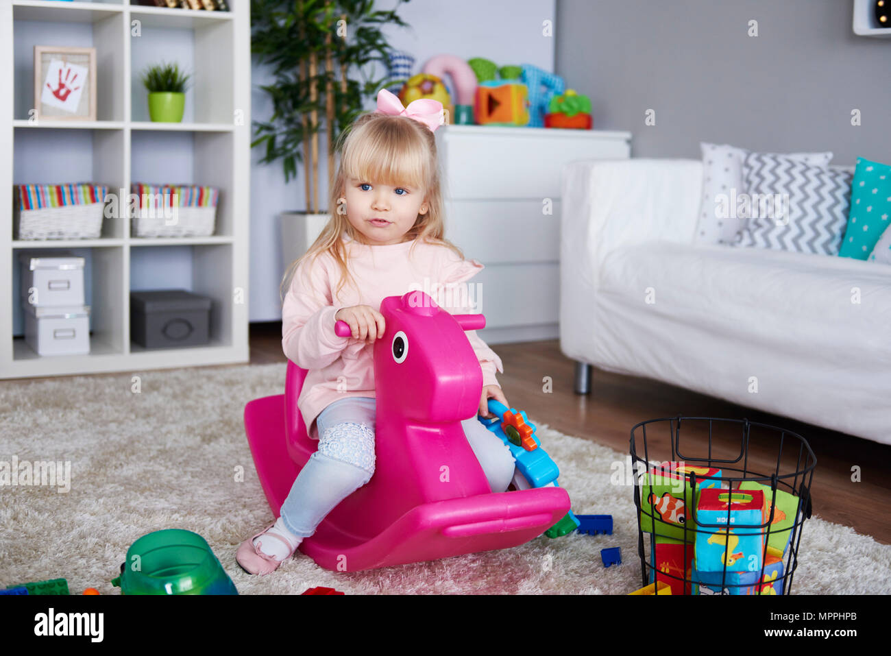 Ritratto di bambina seduta sul rosa cavallo a dondolo in salotto Foto Stock