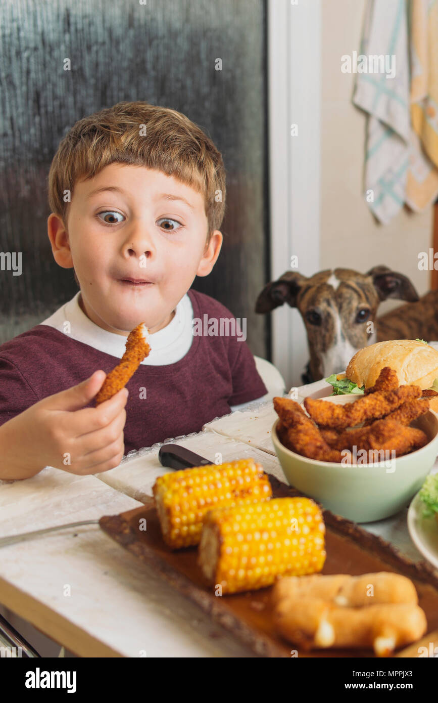 Ragazzo con cane gustando piatti americani al tavolo da pranzo a casa Foto Stock