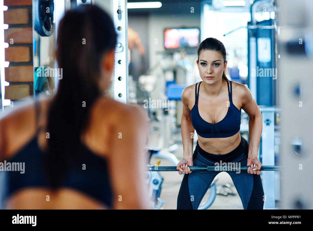 Sollevamento donna barbell in palestra cercando in specchio Foto Stock