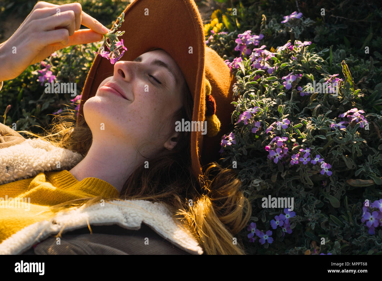 Donna sdraiata nel prato godendo la fragranza di un fiore Foto Stock
