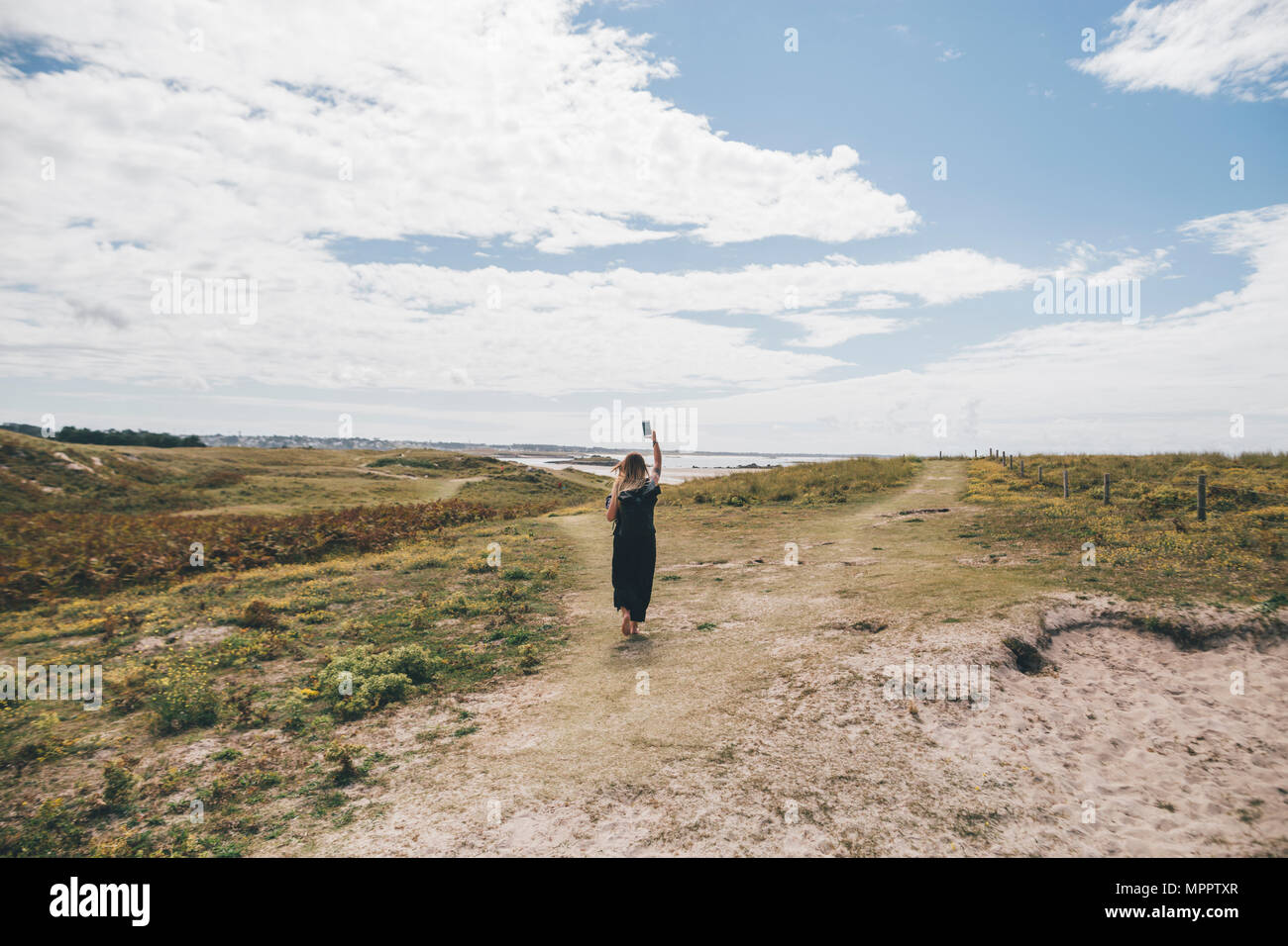 Francia, Bretagna, Landeda, Dune de Sainte-Marguerite, giovane donna camminando sulle dune presso la costa azienda telefono cellulare Foto Stock