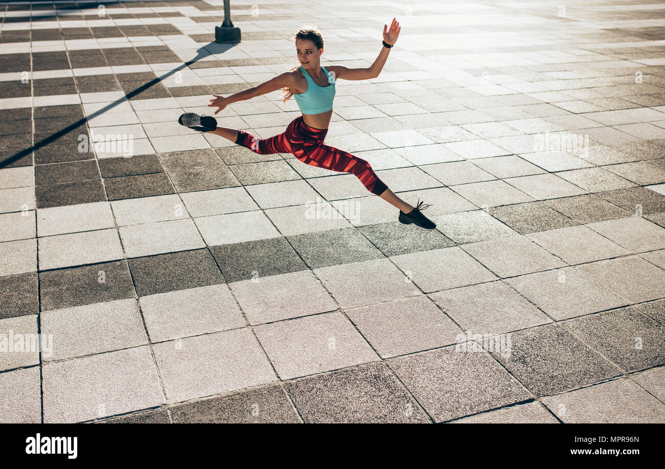 donna fitness che fa split jump all'aperto in città. Atleta flessibile che si allena all'aperto. Foto Stock
