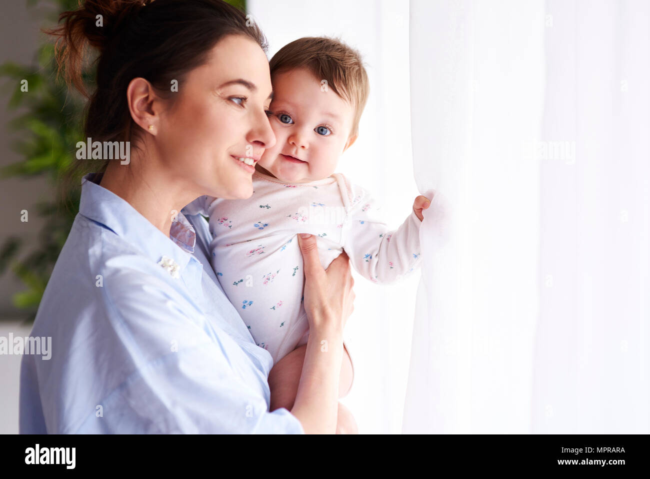 La madre che porta il suo bambino alla finestra home Foto Stock