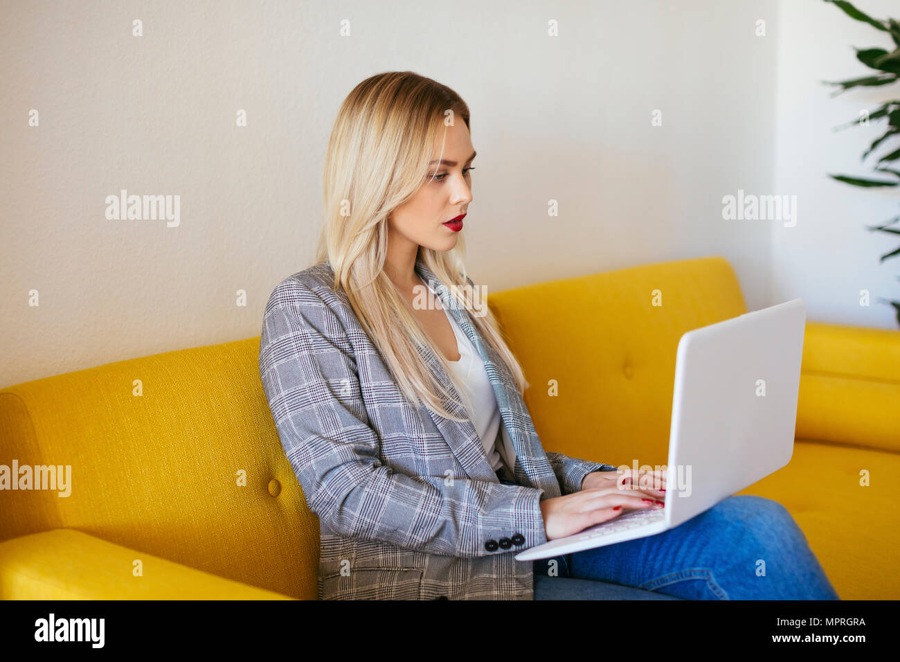 Imprenditrice seduta sul divano giallo, utilizzando laptop Foto Stock