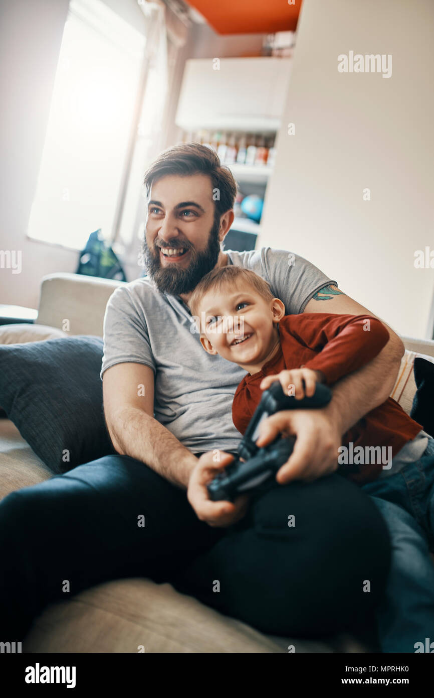 Ridendo padre e figlio seduti insieme sul lettino la riproduzione di giochi per computer Foto Stock