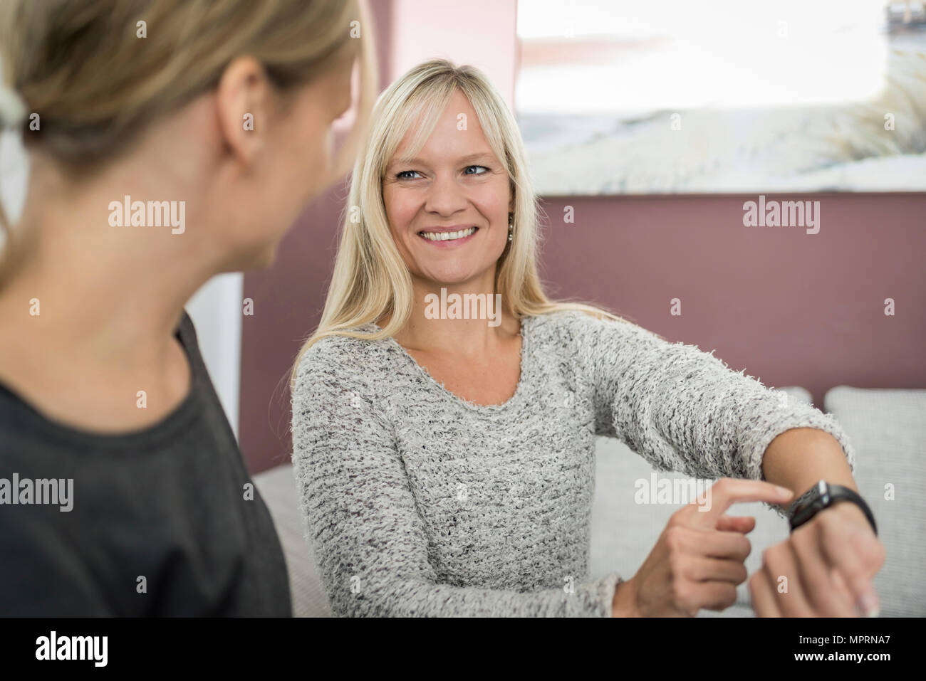 Donna sorridente che mostra smartwatch ad un amico Foto Stock