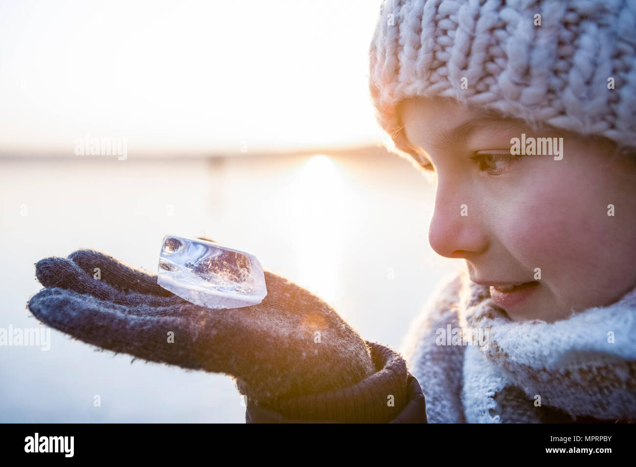 La Germania, il Land Brandeburgo, Lago Straussee, ritratto di una ragazza in piedi sul lago ghiacciato, guardando il pezzo di ghiaccio sulla sua mano Foto Stock