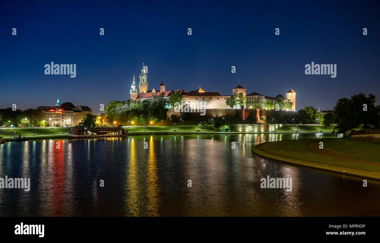 La Polonia, Cracovia. Illuminata castello reale di Wawel e Cattedrale di notte e i riflessi di luce nel fiume Vistola. Riverside con park, alberi, promenade, l Foto Stock
