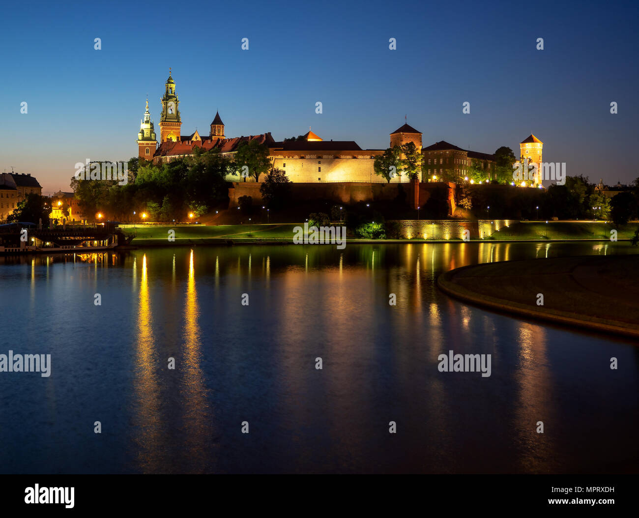 La Polonia, Cracovia. Illuminata castello reale di Wawel e Cattedrale di notte e i riflessi di luce nel fiume Vistola. Riverside con park, alberi, promenade, l Foto Stock