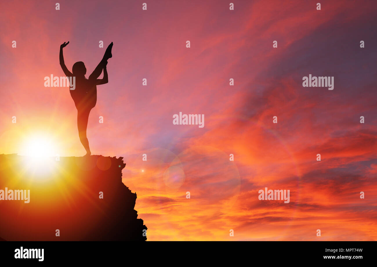 Silhouette di una ragazza che esercitano o stiramento sul bordo della scogliera con drammatico tramonto o l'alba di sfondo e copiare lo spazio. Concetto di stile di vita sano. Foto Stock