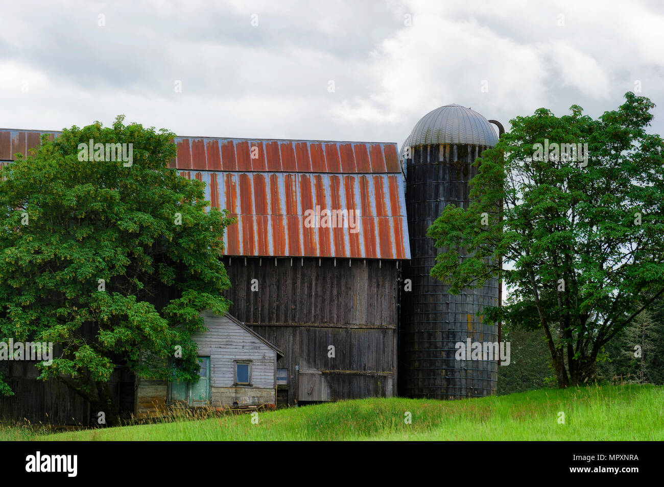 Vista del paesaggio di un vecchio fienile e silo sul pendio di una collina sotto il cielo nuvoloso. Foto Stock
