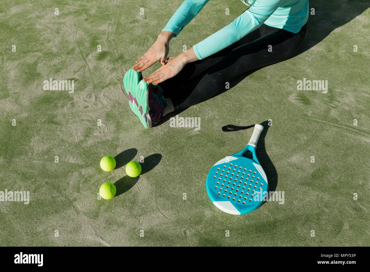 Sezione bassa di donna stretching con la racchetta da tennis e le sfere sulla corte durante la giornata di sole Foto Stock