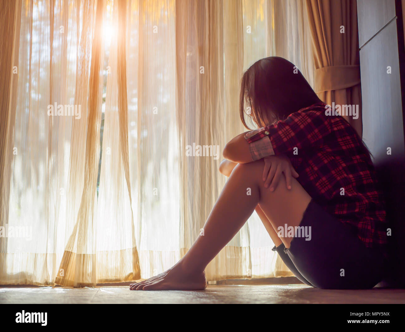 Triste donna abbraccio il suo ginocchio e grido. mentre è seduto da solo in una stanza vuota accanto alla finestra o porta. Foto Stock