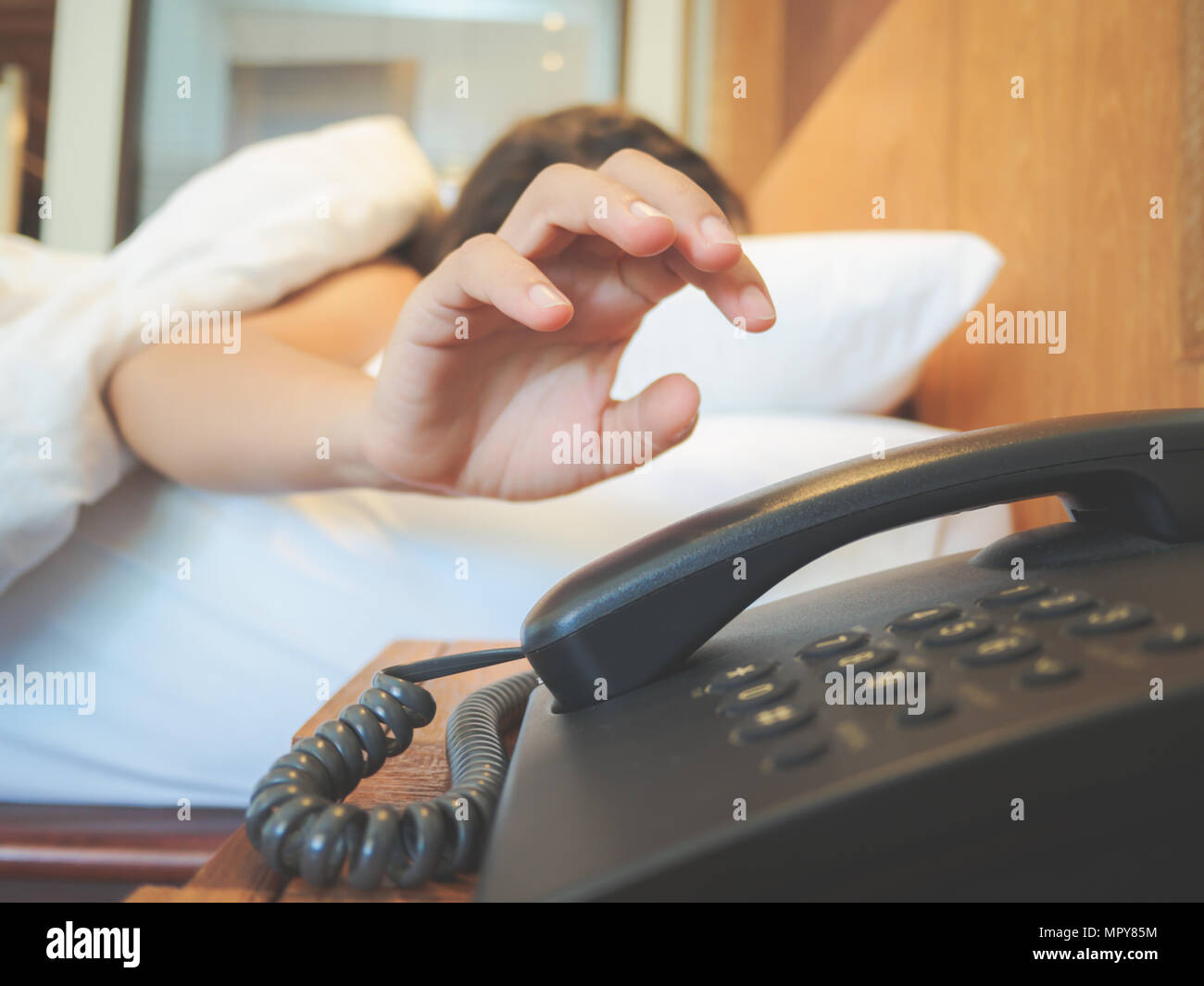 Donna che dorme nel letto di essere svegliati dal telefono, la messa a fuoco a portata di mano. Lazy giorno lavorativo concetto. Foto Stock