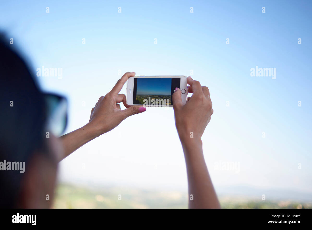 Tagliate le mani della donna di fotografare con il cellulare contro il cielo chiaro Foto Stock