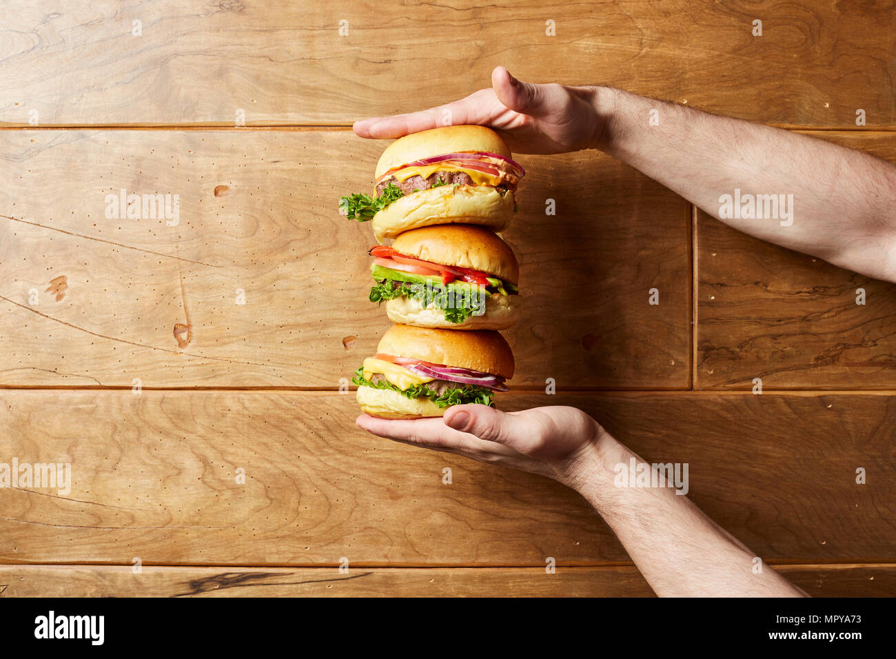 Tagliate le mani dell uomo holding cheeseburger su un tavolo di legno Foto Stock