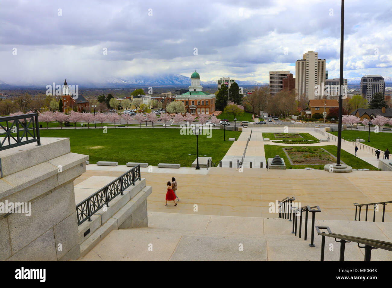Ragazza in abito rosso a piedi lungo la capitale dello stato dello Utah A Salt Lake City. Il fiore di ciliegio alberi sono in piena fioritura di primavera Foto Stock