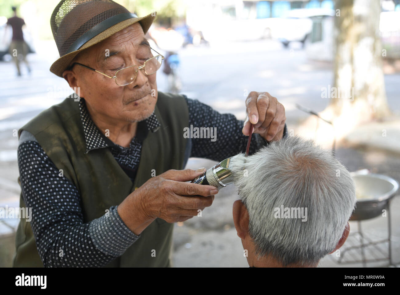 Nanjin, Nanjin, Cina. Xxiv Maggio, 2018. Nanjing, Cina-24Maggio 2018: Il 79-year-old street barbiere Wang Xiaofu taglia i capelli per un uomo sulla strada di Nanjing East cinese della provincia di Jiangsu. Wang ha iniziato a imparare barbery all'età di 13 ed è stata una strada barbiere per 66 anni. Credito: SIPA Asia/ZUMA filo/Alamy Live News Foto Stock
