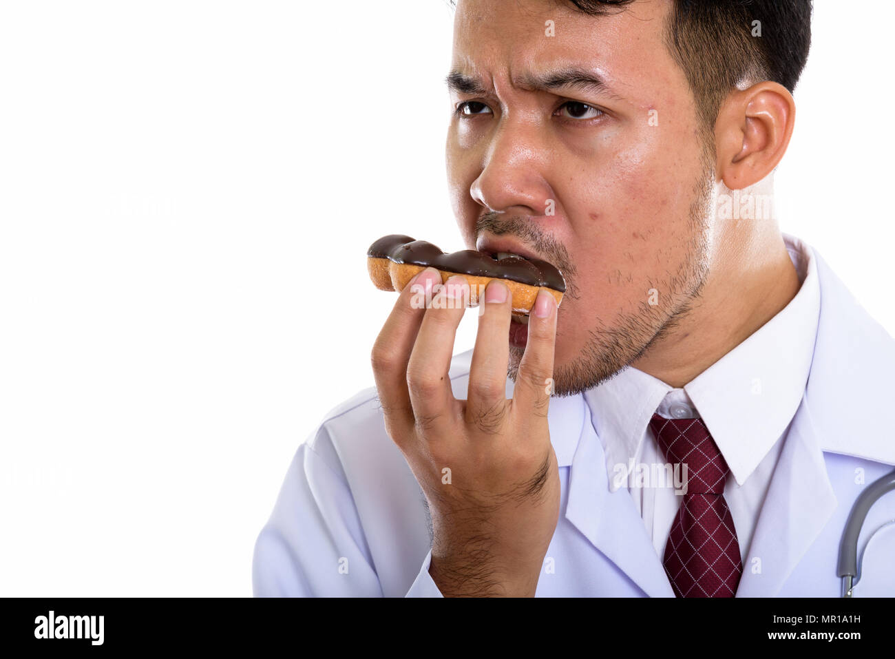 Chiusura del giovane uomo asiatico medico mangiare donut e pensare Foto Stock