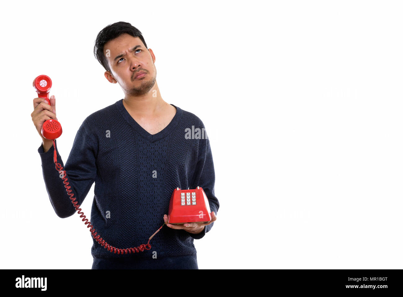 Studio shot del giovane uomo asiatico tenendo il vecchio telefono alla ricerca ann Foto Stock